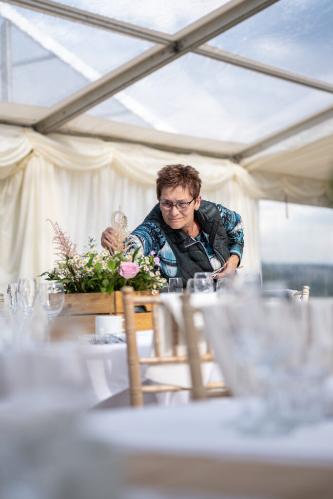 Hochzeitsdekoration im Festzelt – Frau arrangiert Blumenschmuck auf einem Hochzeitstisch in England, festgehalten von Hochzeitsfotograf Björn Stuhr.